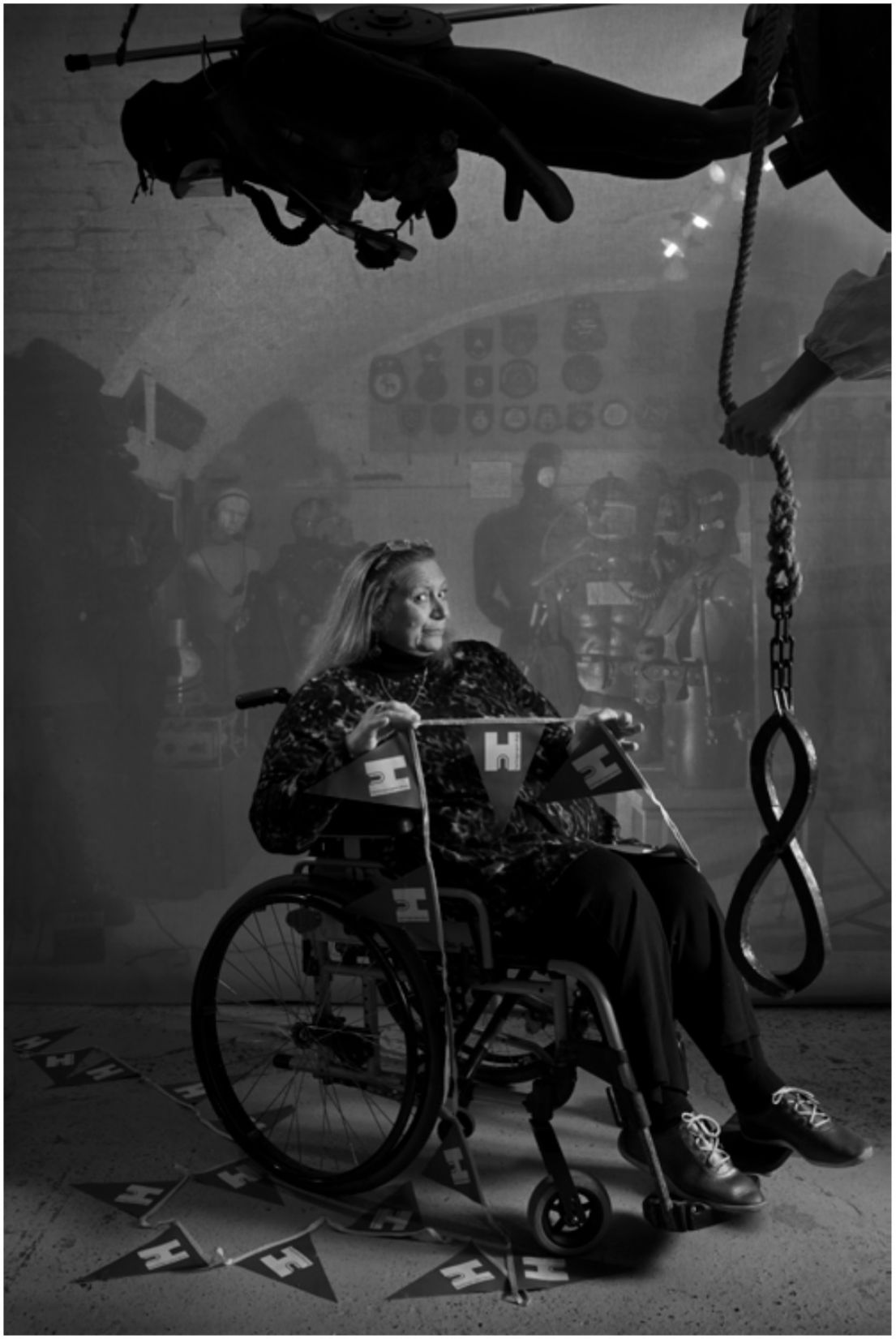 A black and white photo of a woman sat in a wheelchair, holding up the HODs bunting.
