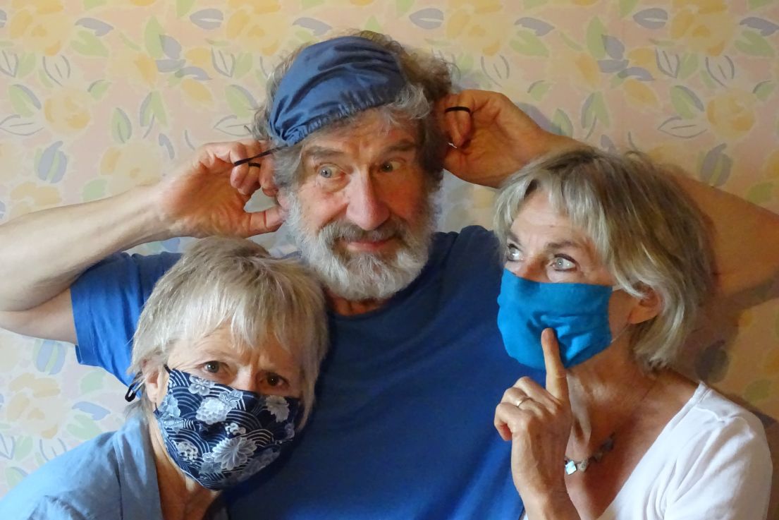Three people, one man and two women, joking around wearing fabric blue face masks.