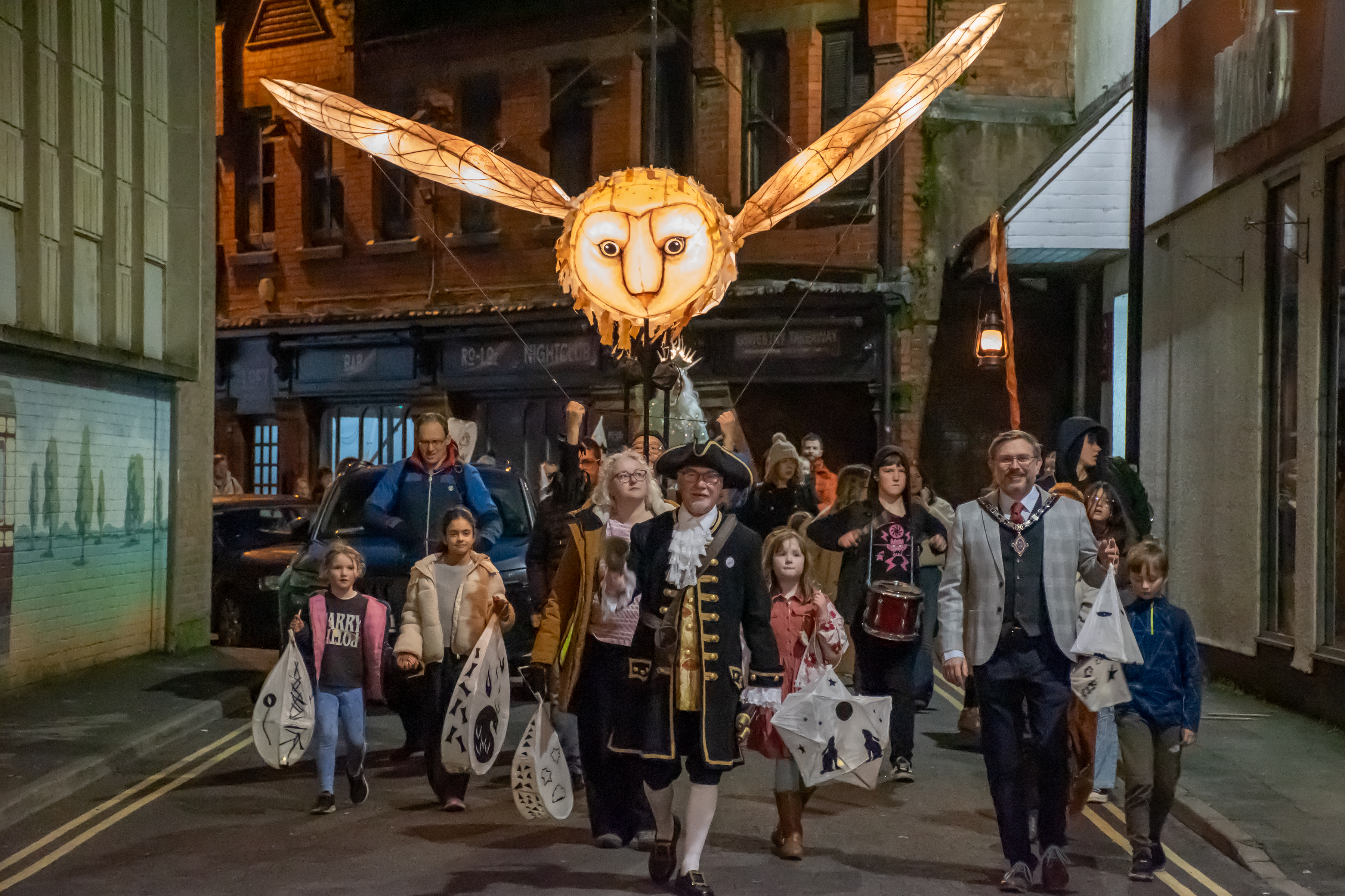 Group of people walking down a street in Oswestry under a large lantern of an owl