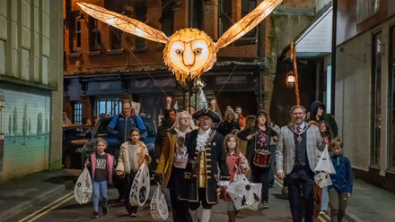 Group of people walking down a street in Oswestry under a large lantern of an owl