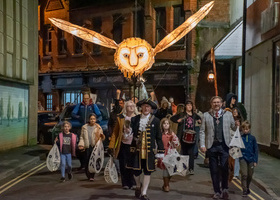 Group of people walking down a street in Oswestry under a large lantern of an owl