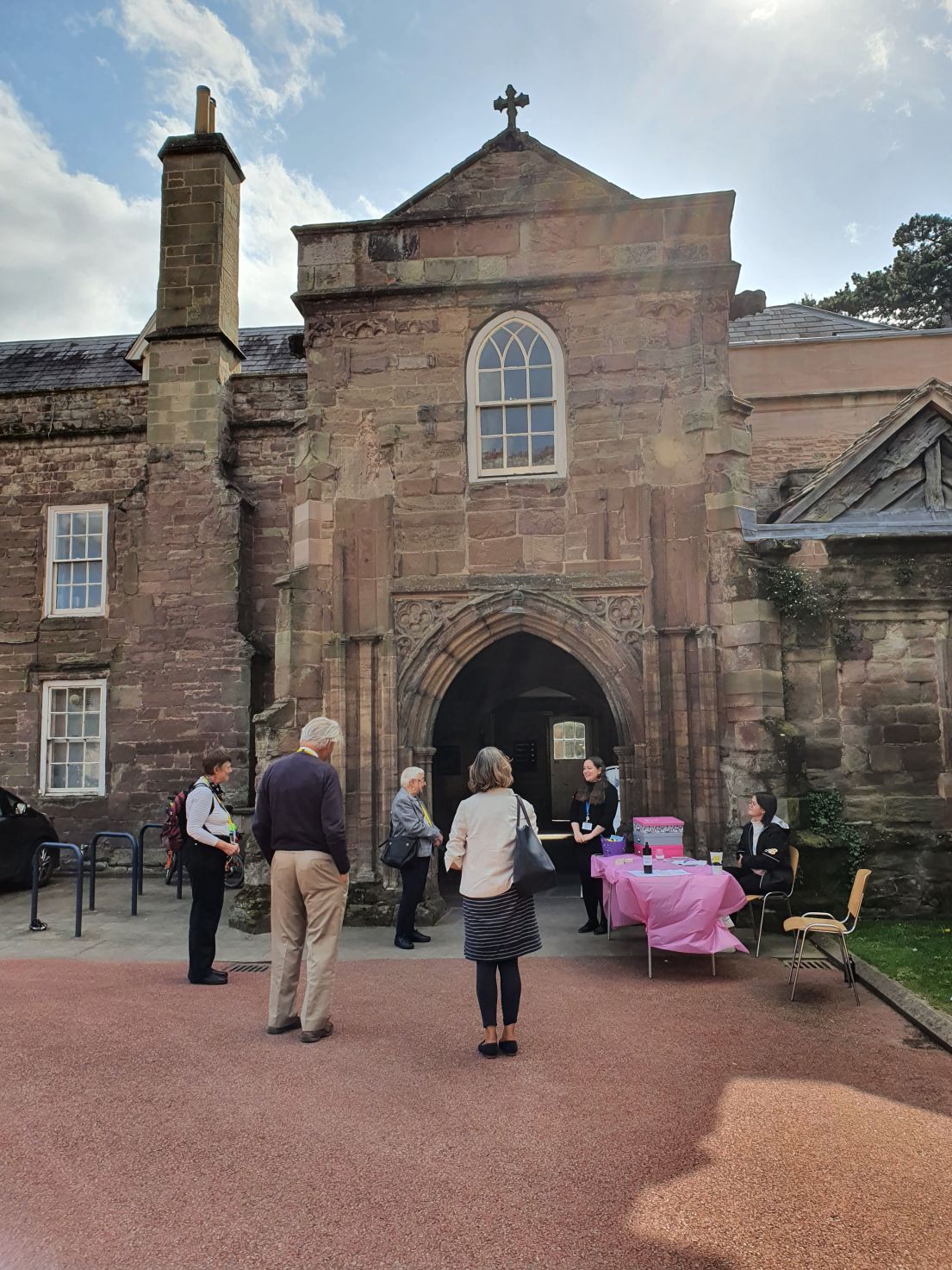 People walking up to an archway in a building, a table with pink table cloth is on the outside.