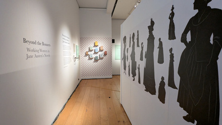 Exhibition wall with silhouettes of Georgian era women lining a short, wooden floored, corridor.