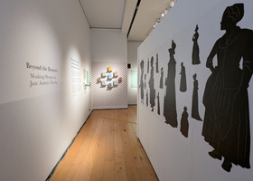 Exhibition wall with silhouettes of Georgian era women lining a short, wooden floored, corridor.