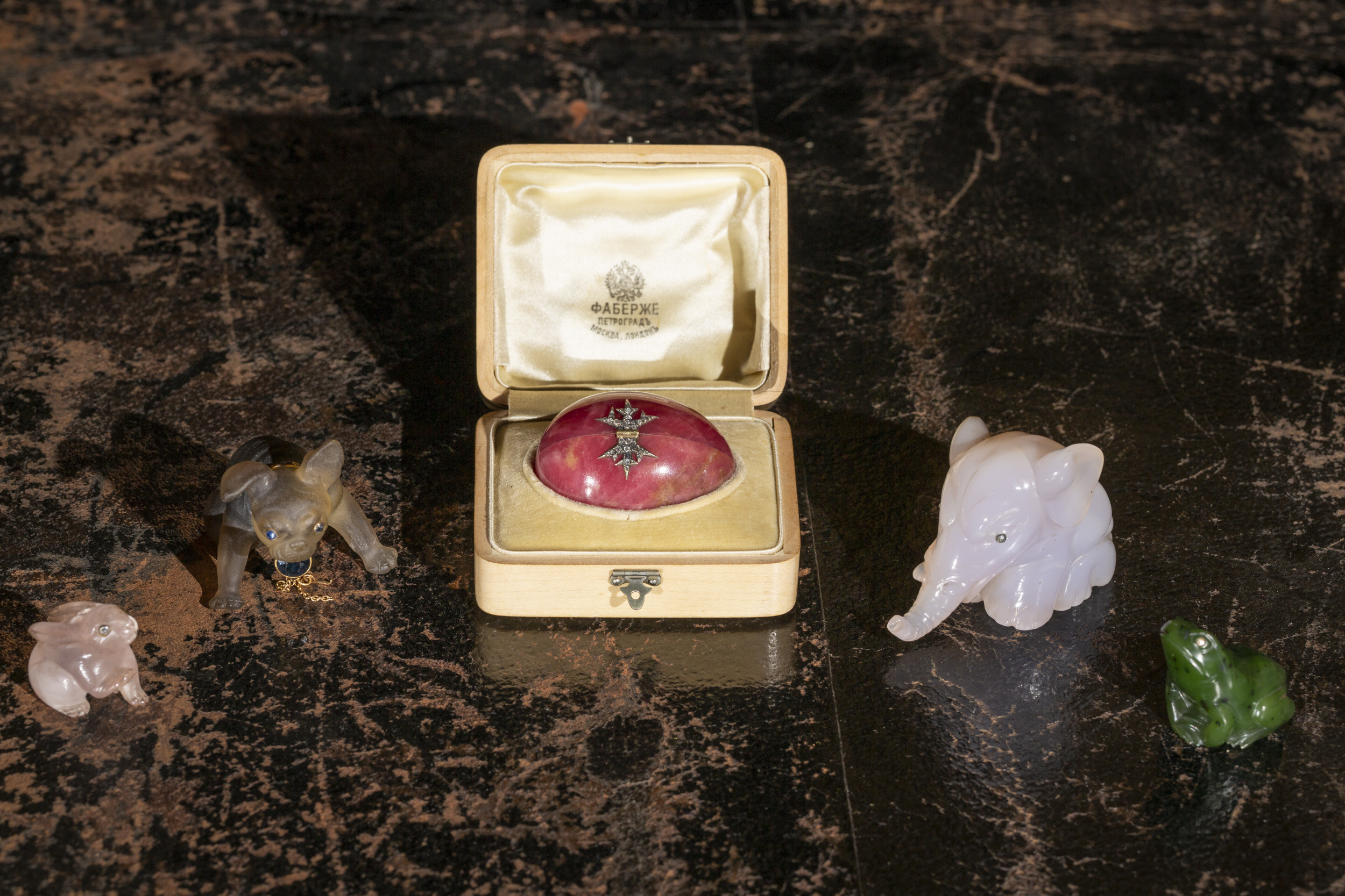 Small box holding a pink egg with two carved animals on either side including an elephant and a frog.