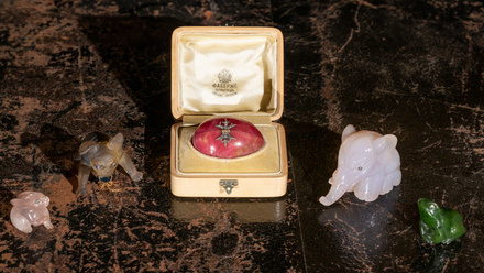 Small box holding a pink egg with two carved animals on either side including an elephant and a frog.