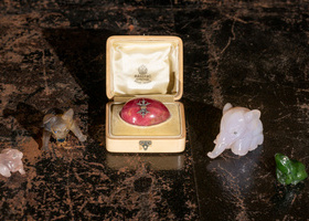 Small box holding a pink egg with two carved animals on either side including an elephant and a frog.